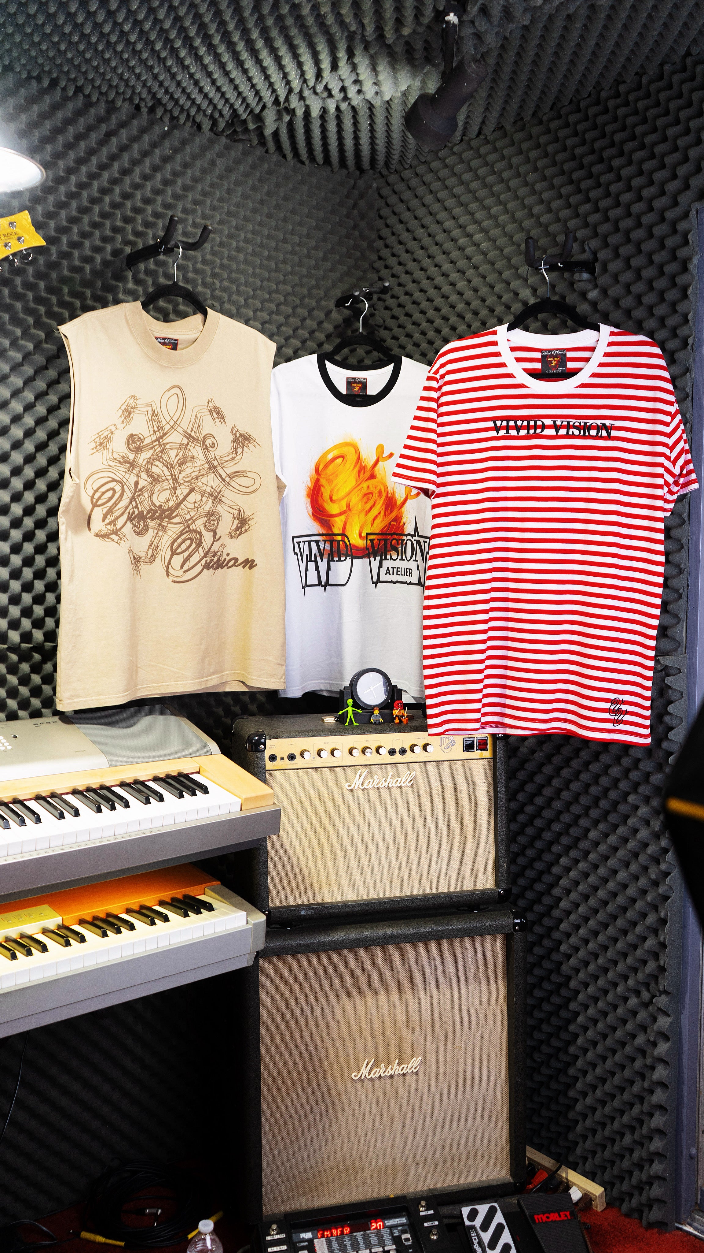 Three t-shirts hanging on a rack with musical equipment below.