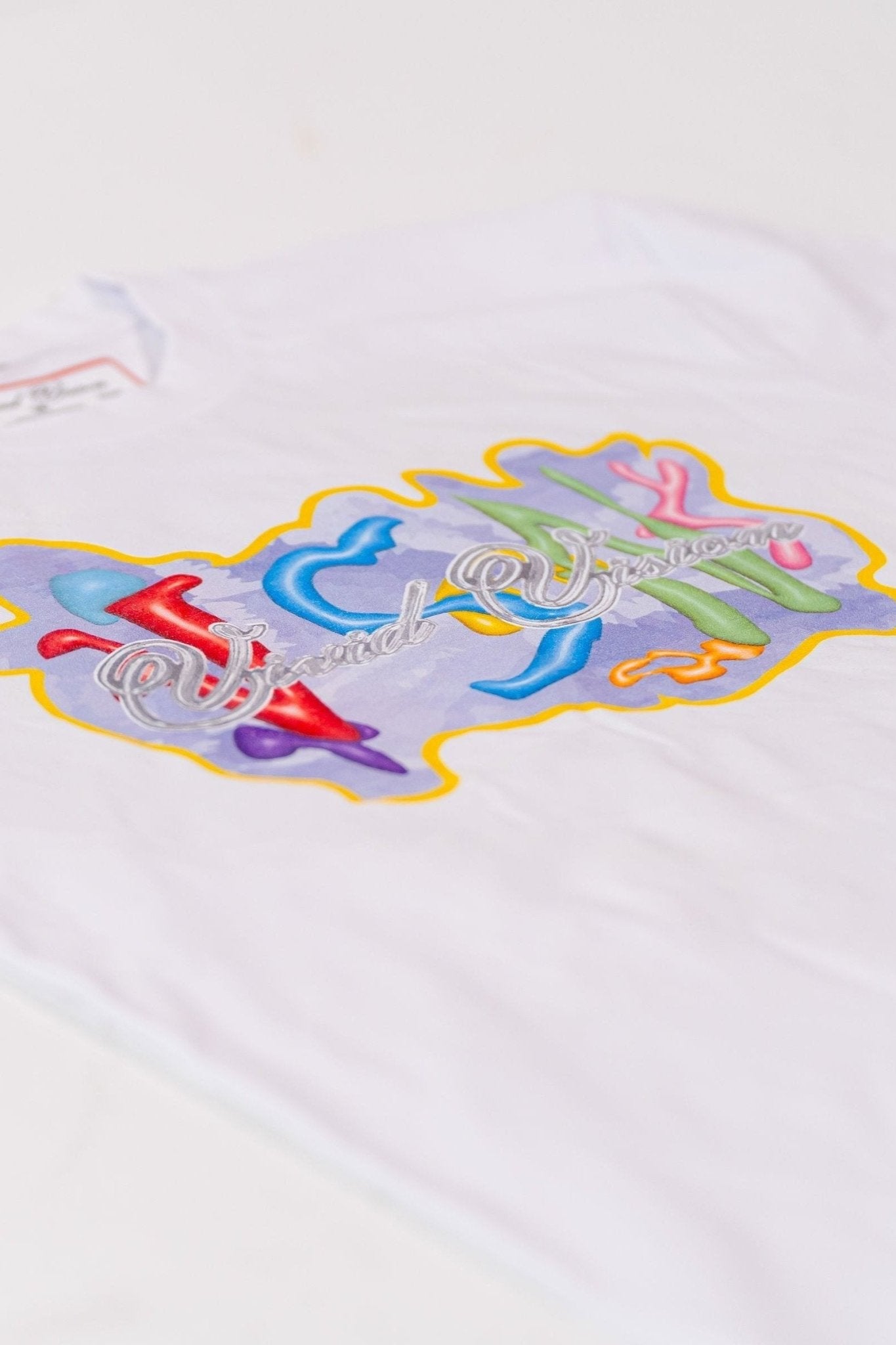 A flat lay of a white T-shirt with colorful graffiti-style text design on the front.